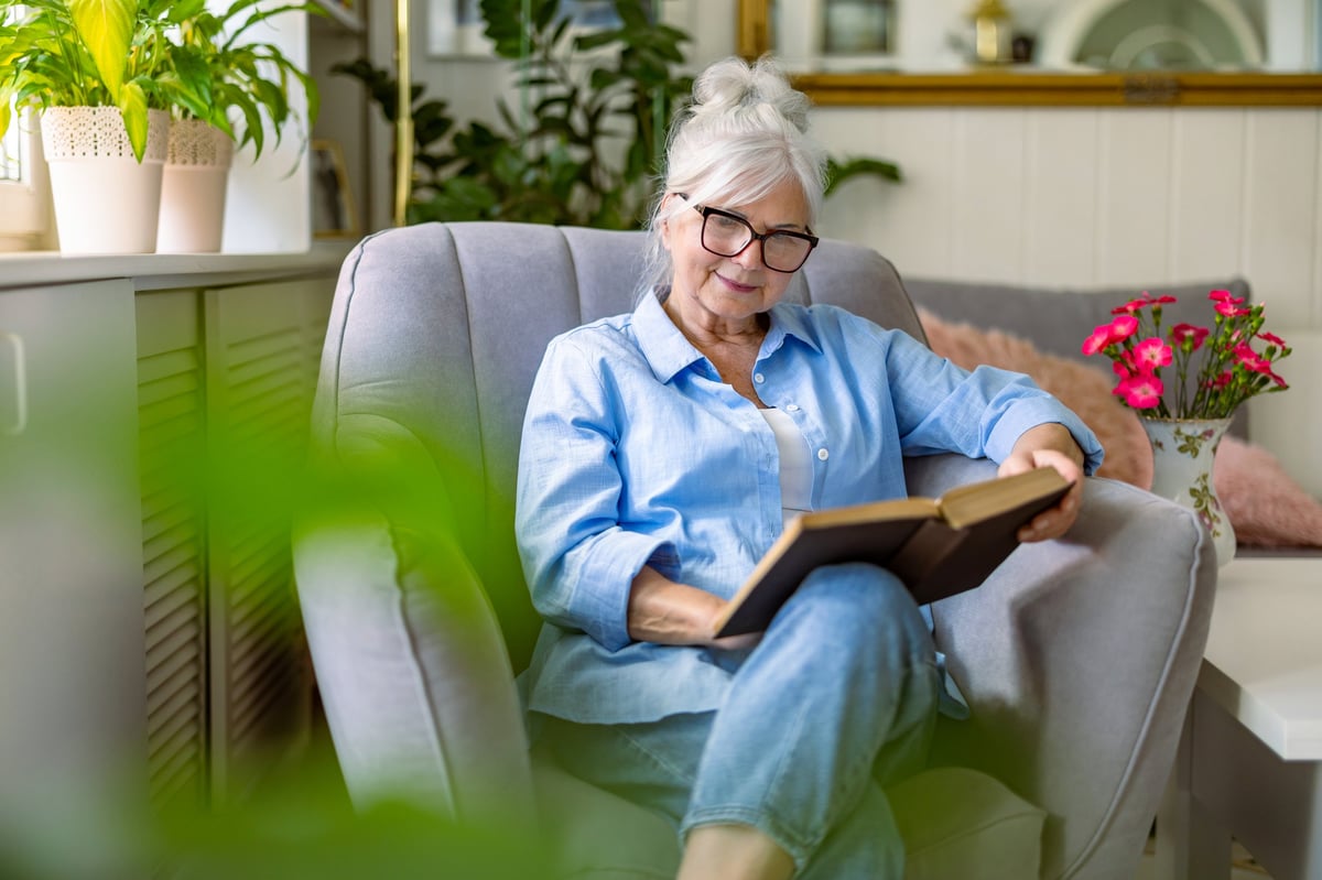 A woman in her late sixties reading in a comfortable armchair at home