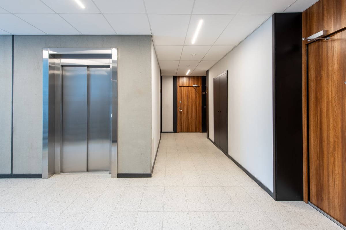 A quiet residential corridor with warm timber doors and soft daylight along the floor