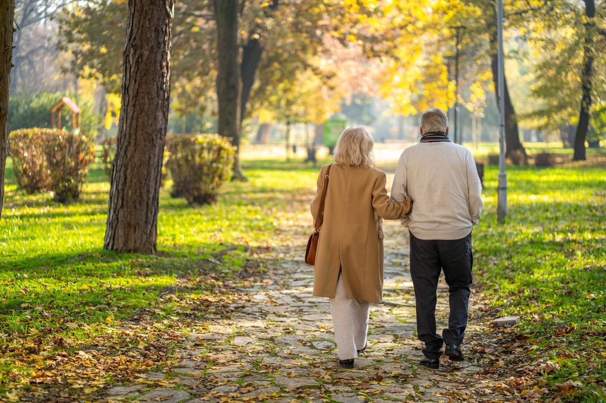 An older couple walking arm in arm along a path on a clear autumn day