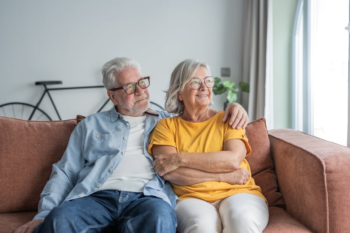 A retired couple sitting together on the sofa in the home they have owned for years