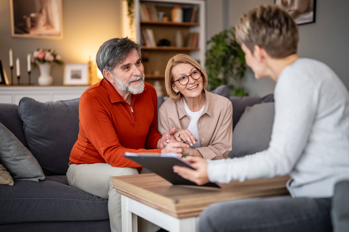 A couple holding hands while talking with an advisor in their living room